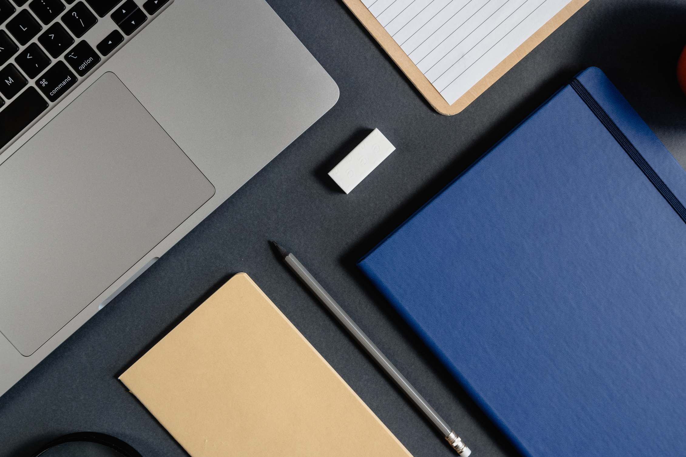 Overhead view of a desk with laptop and notes for a testing engagement, minimalist office stationery on a dark surface
